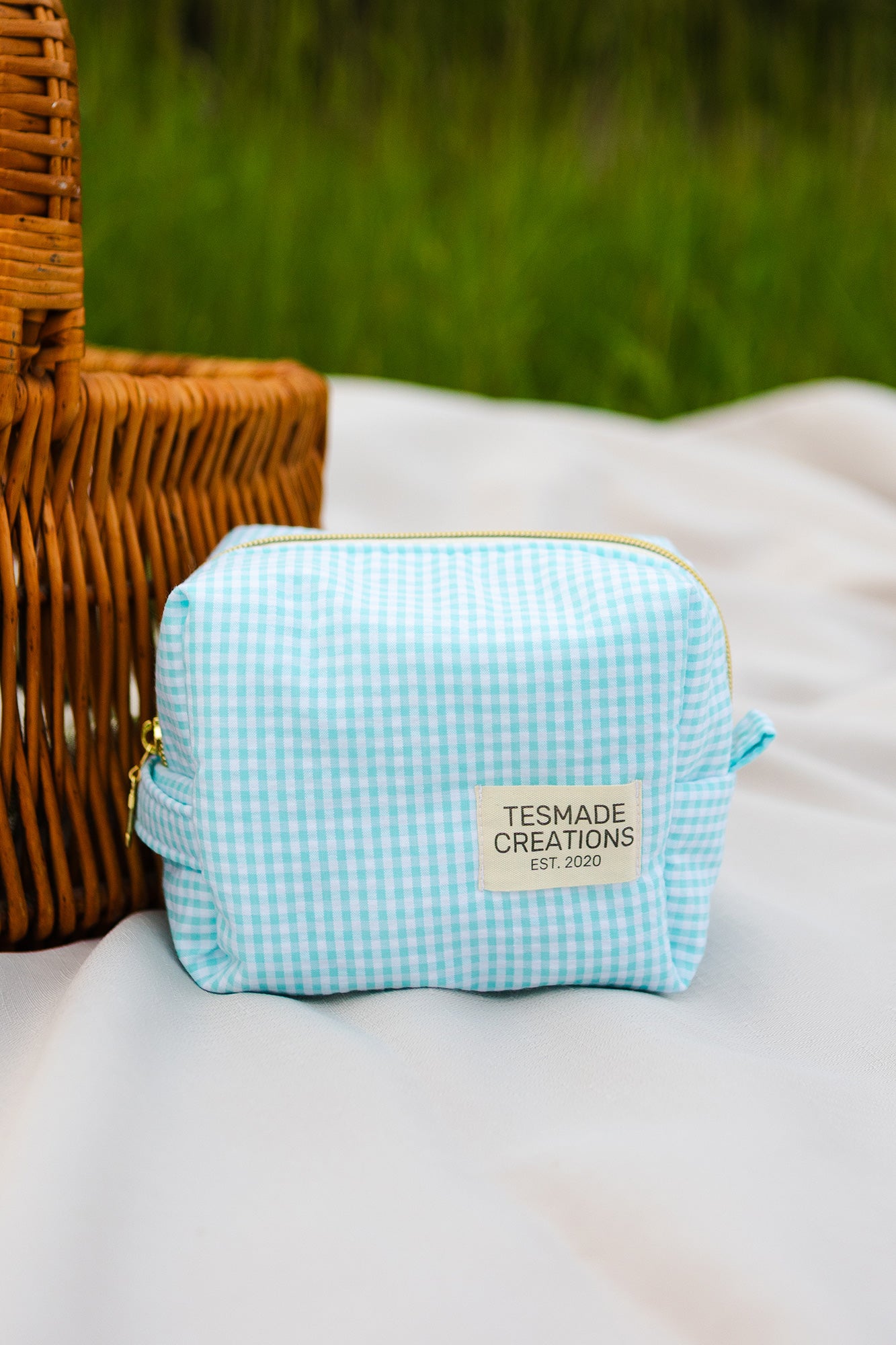 Light blue gingham pouch with 'TESMADE CREATIONS' label on a white surface with a blurred green background