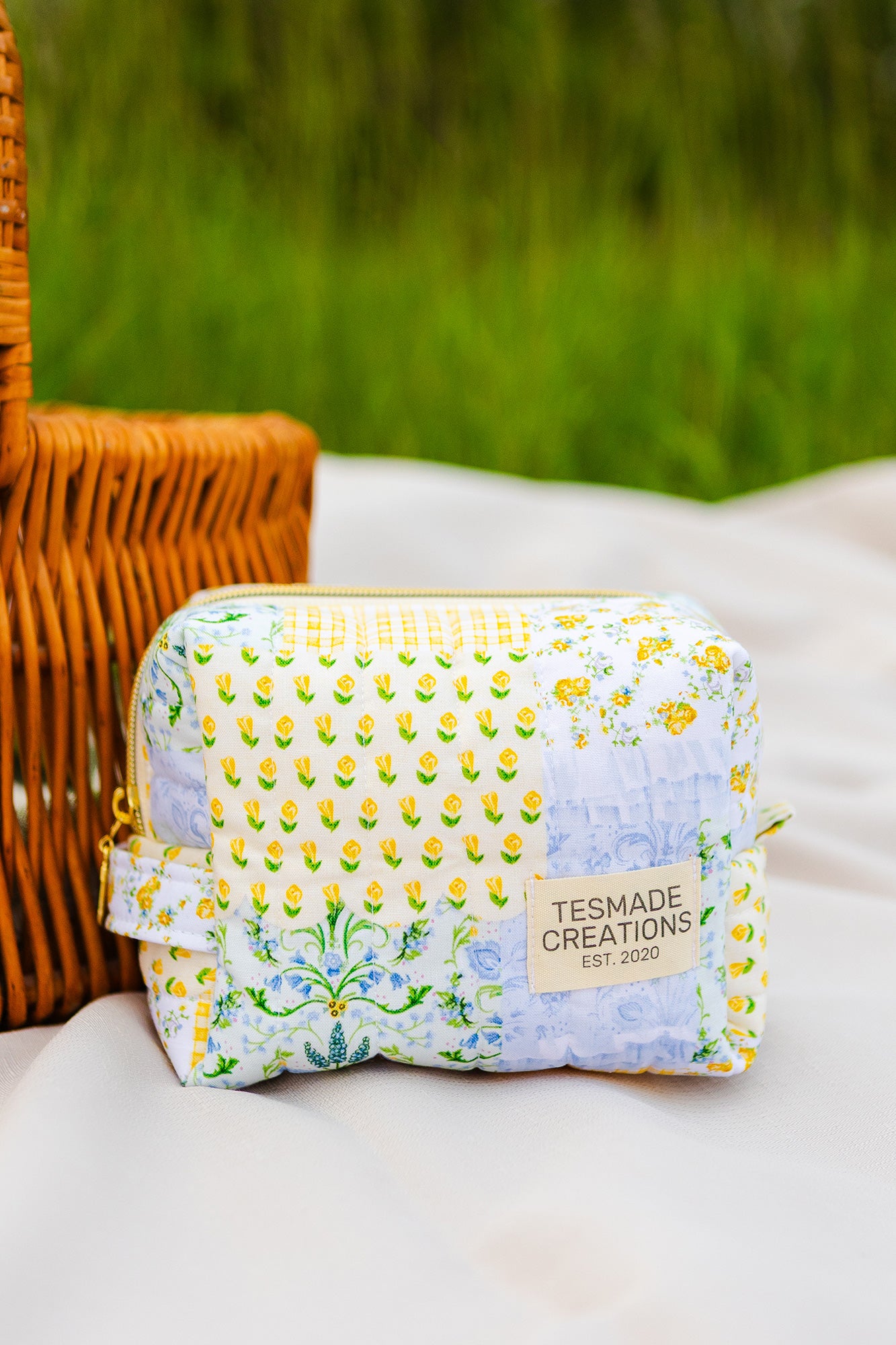 Fabric pouch with floral pattern and 'Tesmade Creations' label on a white surface with green grass in the background.