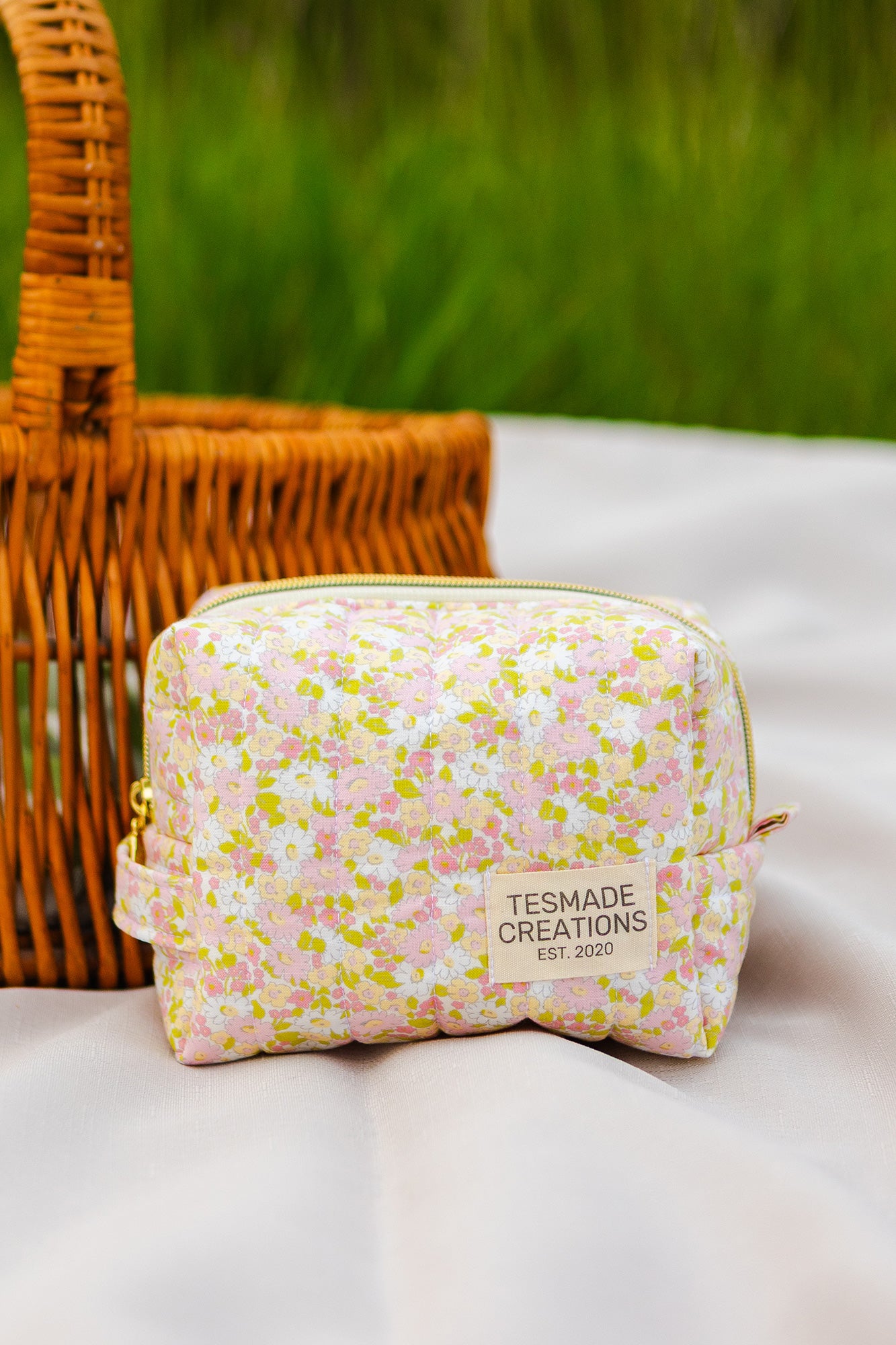 Floral-patterned pouch with 'Tesmade Creations' label on a white surface with a wicker basket in the background.