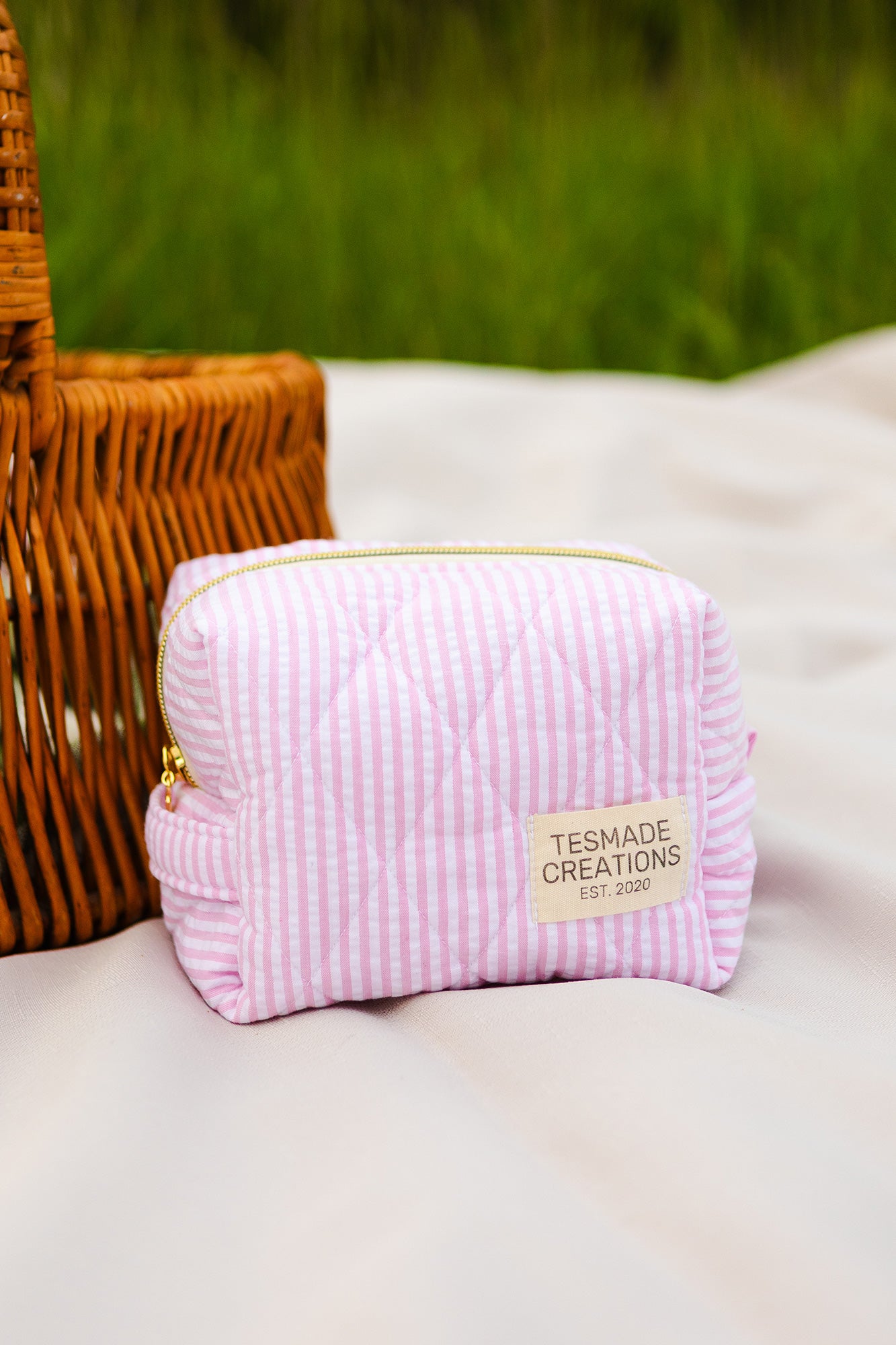 Pink striped pouch with 'Tesmade Creations' label on a white surface with a blurred green background