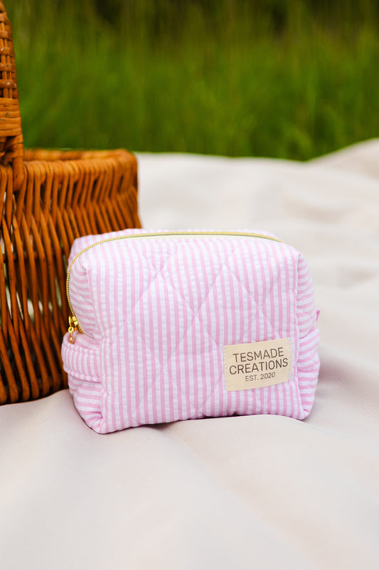 Pink striped pouch with 'Tesmade Creations' label on a white surface with a blurred green background