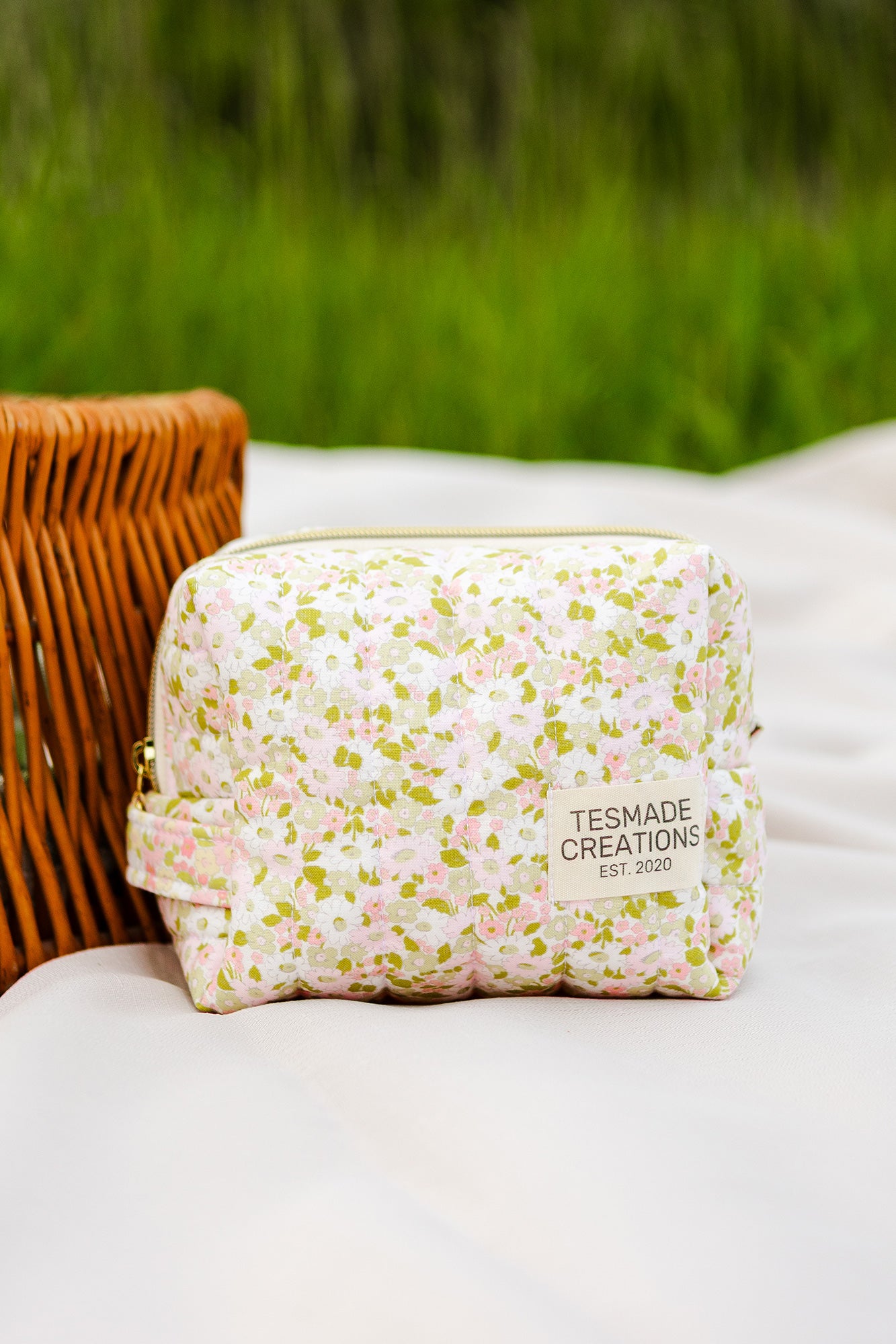 Floral-patterned pouch with 'TESMADE CREATIONS' branding on a white surface with grass in the background
