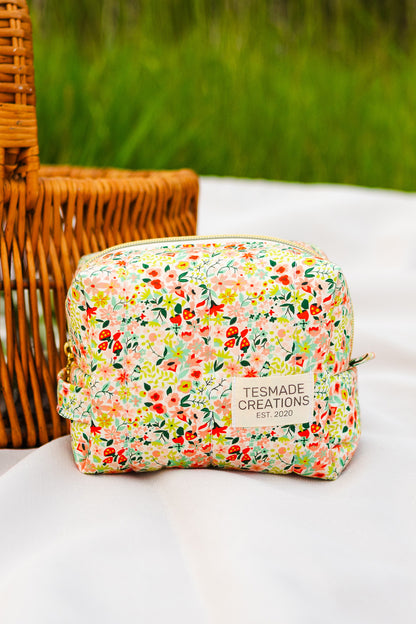 Floral-patterned pouch with 'Tessmade Creations' branding on a white surface with a wicker basket and greenery in the background.