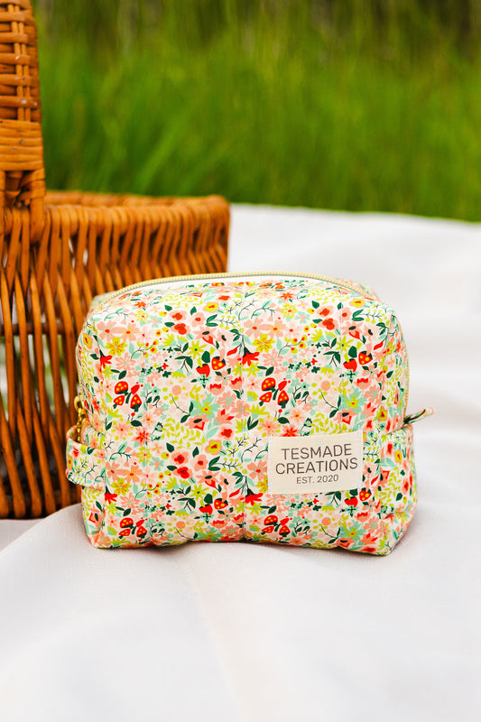 Floral-patterned pouch with 'Tessmade Creations' branding on a white surface with a wicker basket and greenery in the background.