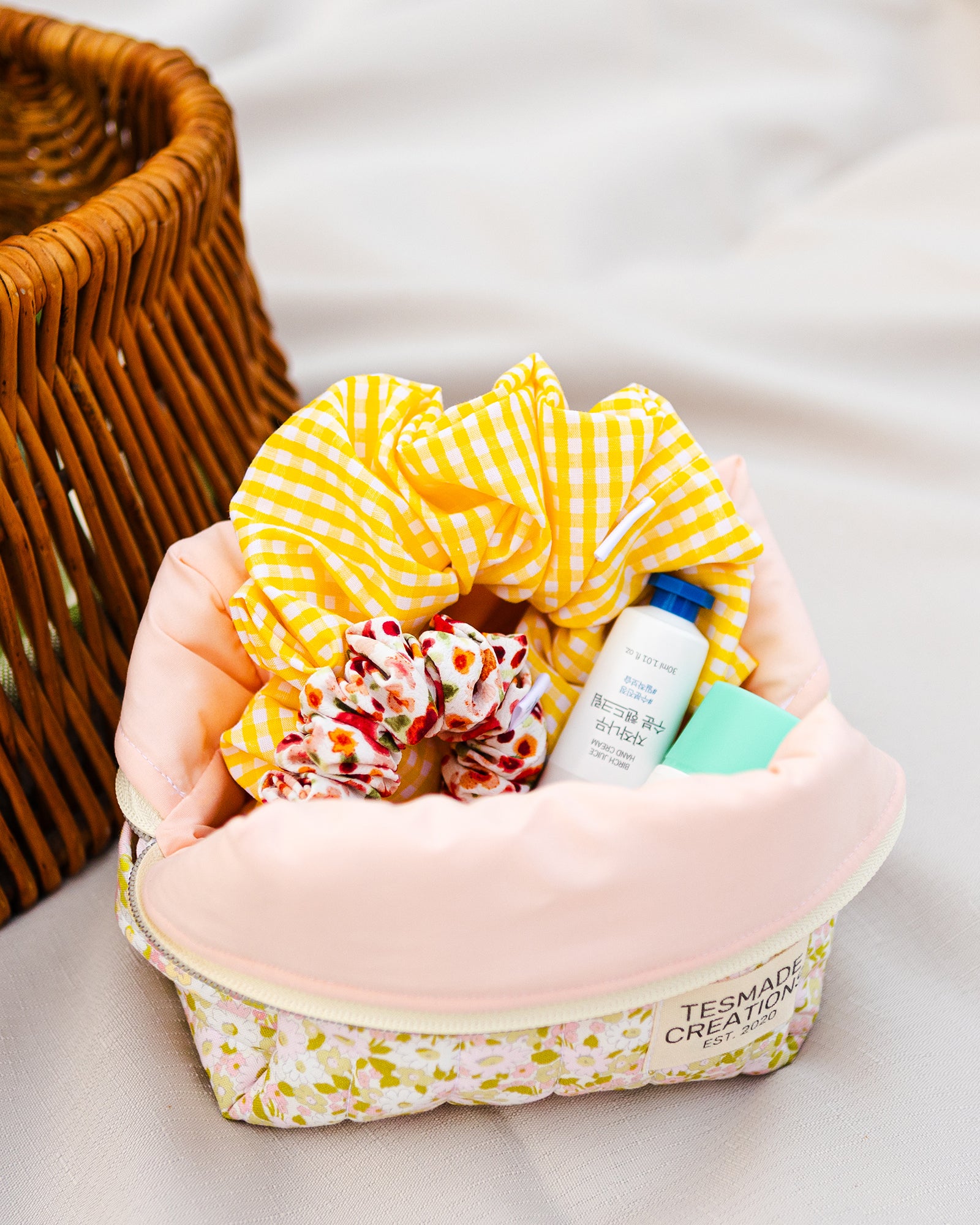 Green floral cosmetic bag with pink fabric interior with yellow checkered towel, hair products on a light background.