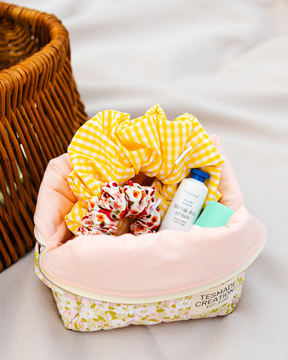 Green floral cosmetic bag with pink fabric interior with yellow checkered towel, hair products on a light background.
